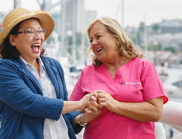 A happy Nurse Next Door caregiver walking with a woman while laughing